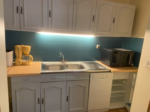 Petite cuisine de l'appartement Hôtel De La Bonnheur avec armoires blanches, crédence carrelage bleu-vert et évier inoxydable
