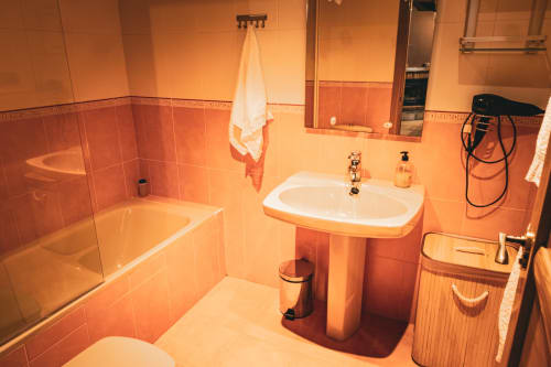 Baño con azulejos naranjas, bañera, lavabo sobre pedestal e inodoro en Casa Rural Sensaciones de Cuevas de Viñayo