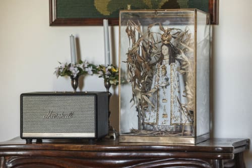 Elegante altar en la recepción de Casa das Jardas con cuadros religiosos enmarcados, velas y altavoz Marshall.