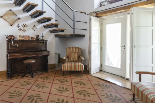 Elegante salón de Casa das Jardas con piano, butaca a rayas y escalera flotante en Ladoeiro