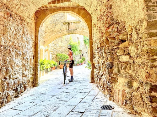 Ciclista amb bicicleta en un passatge medieval amb arcs de pedra, L'Estartit, Catalunya