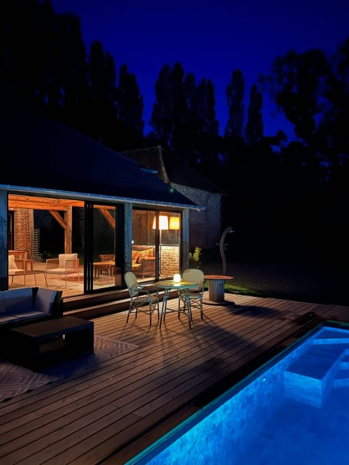 Domaine de Blanvatel evening patio with illuminated pool, deck seating, and glowing stone cottage