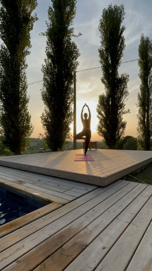 Person in yoga pose on wooden platform surrounded by tall poplar trees at sunset, Domaine de Blanvatel, Saint Pierre en Auge