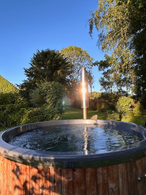 Hot tub at Domaine de Blanvatel with sunset, surrounded by garden trees in Saint Pierre en Auge