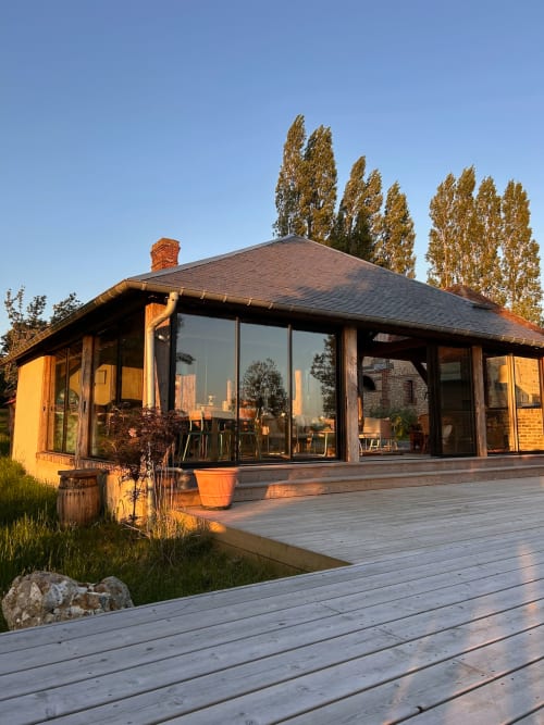 Modern wooden pavilion at Domaine de Blanvatel B&B in Saint Pierre en Auge with glass walls, deck, and poplar trees at sunset