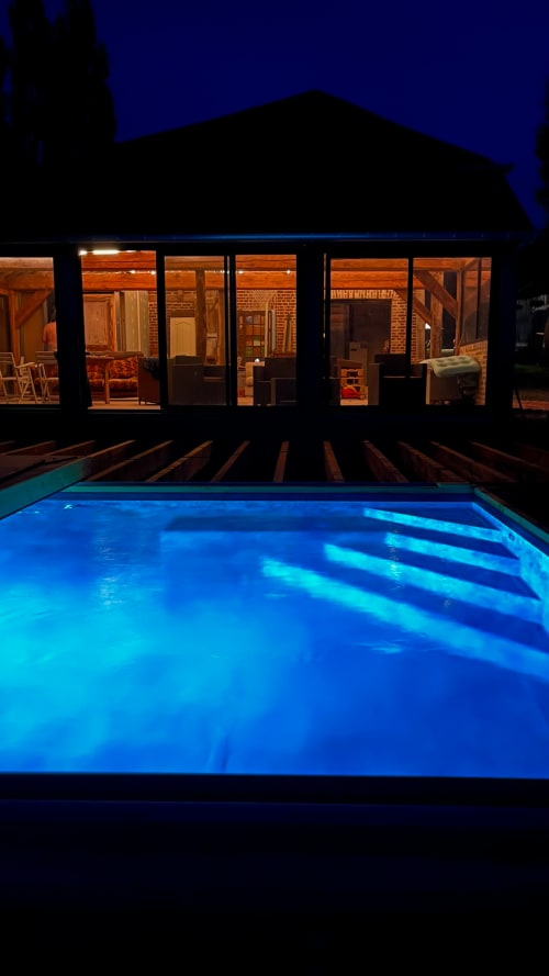 Illuminated swimming pool at night with warm-lit brick house at Domaine de Blanvatel B&B, Saint Pierre en Auge