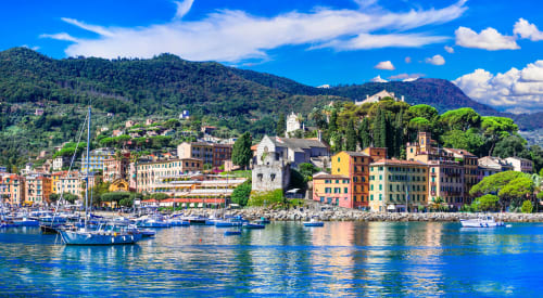 Edifici colorati sul waterfront dell'Hotel Bel Sit a Rapallo, Italia con barche a vela e montagne