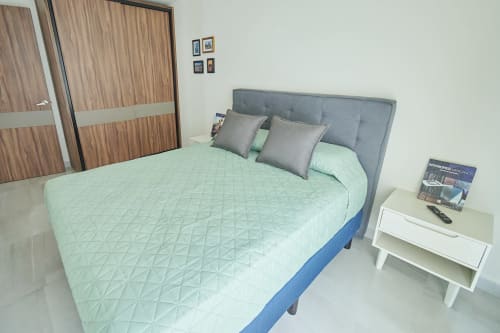Moderna recámara en apartamento Pares Homes, CDMX con cama matrimonial, cabecera gris, ropa de cama verde menta y buró blanco