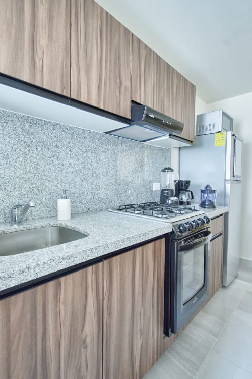 Cocina moderna en departamento Pares Homes CDMX con gabinetes de madera, encimera de granito, estufa a gas y acero inoxidable