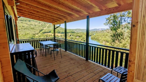 Terrazza coperta del Lodge l'EPERVIER con tavolo da pranzo, sedie a sdraio, vista sul fiume e montagne boscose vicino a Serrières-sur-Ain