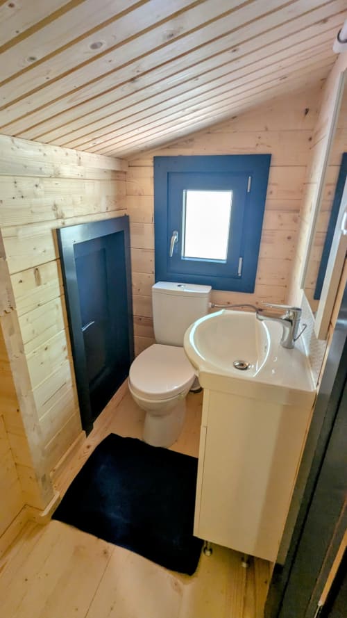 Bagno compatto nel Lodge l'EPERVIER con toilette, lavabo tondo, finestra blu, pareti in legno e tappetino nero
