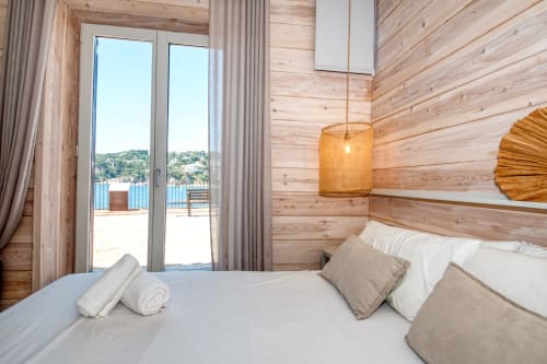 Wooden cabin bedroom with sea views, double bed, pendant light, and patio doors overlooking Mediterranean in Palafrugell