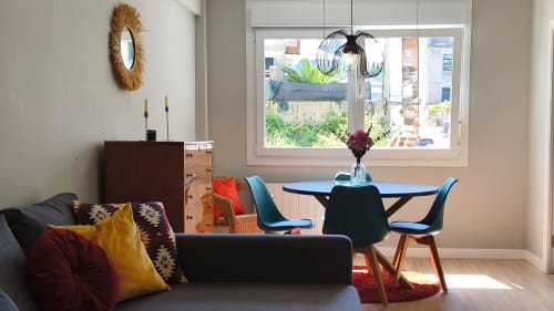 Moderno salón en Baiona con comedor, sillas azules, sofá negro con cojines coloridos y vistas al jardín