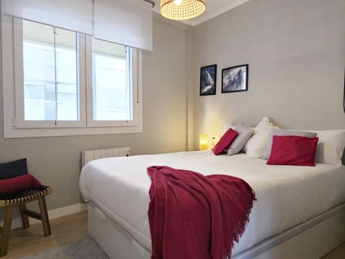 Dormitorio moderno en Holibai Baiona con cama blanca, almohadas rojas, vistas a la ciudad y decoración contemporánea