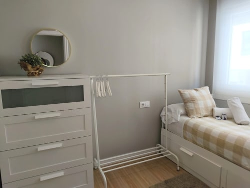 Habitación luminosa en Holibai Baiona con cama blanca, cómoda, espejo redondo y piso de madera