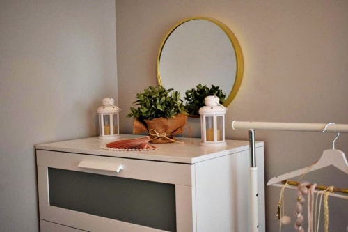 Cómoda moderna con espejo redondo dorado, plantas en maceta, faroles y decoración en Holibai Baiona