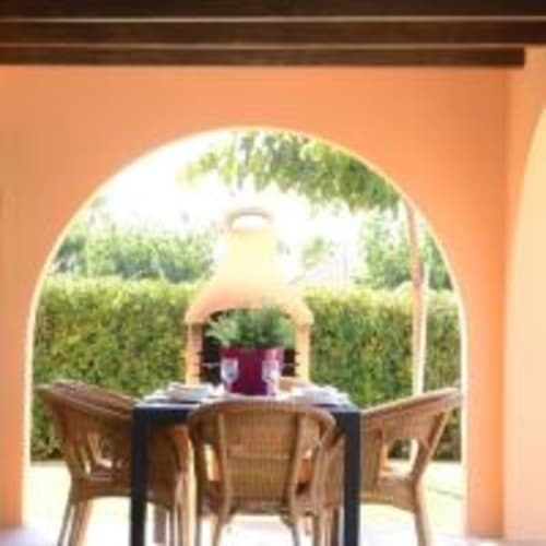 Zona de comedor exterior en la villa Las Golondrinas con entrada arqueada, sillas de mimbre y vistas al jardín en Cap d'Artrutx