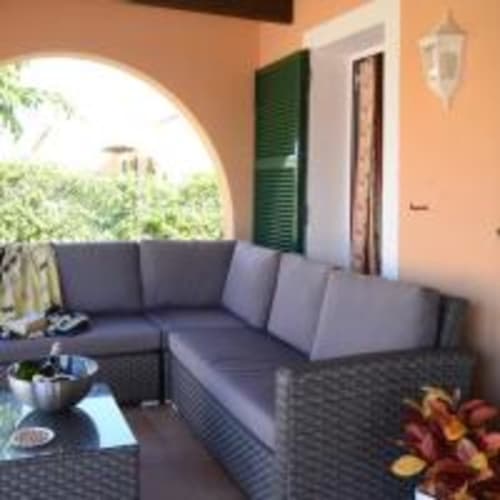 Patio cubierto con sofá de esquina azul y mesa en villa Las Golondrinas, Cap d'Artrutx, con vistas a jardines exuberantes