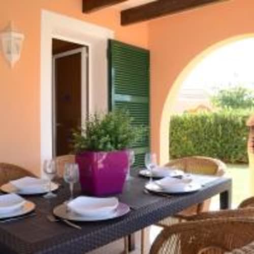 Zona de comedor al aire libre en villa Las Golondrinas con mesas servidas, maceta púrpura y vistas al jardín