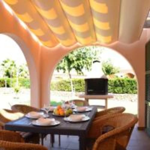 Área de comedor al aire libre en villa Las Golondrinas bajo arco de terracota con vista a la piscina