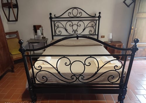 Ornates schwarzes Metallbett mit cremefarbener Bettwäsche im Agri-Bio Santa Palmira, Pomarance, Italien