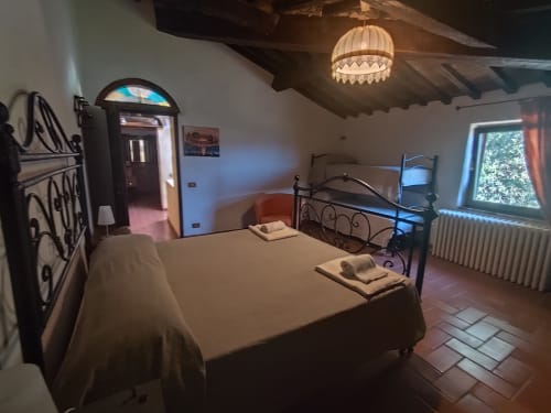 Camera rustica all'Agri-Bio Santa Palmira a Pomarance con letto in ferro battuto, pavimento in cotto e travi di legno a vista.