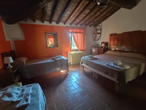 Camera rustica all'Agri-Bio Santa Palmira di Pomarance con pavimenti in cotto, travi di legno a vista e accenti arancioni