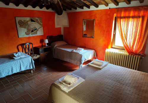 Camera rustica luminosa ad Agri-Bio Santa Palmira a Pomarance con tre letti, pavimento in cotto e vivaci pareti arancioni