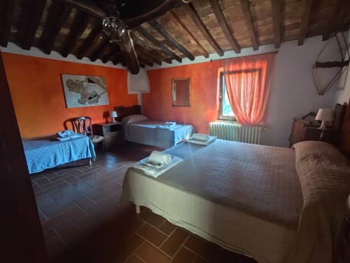 Ampia camera con più letti ad Agri-Bio Santa Palmira, pareti arancioni, travi in legno e biancheria blu a Pomarance