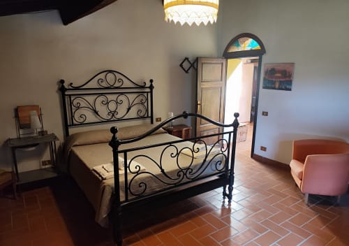 Schlafzimmer des Apartments Santa Palmira mit verziertem Eisenbett, Terrakottaböden und Gartentür bei Agri-Bio Santa Palmira