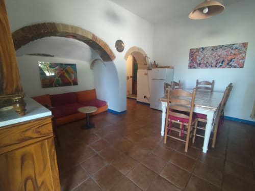 Offene Küche und Essbereich im Agri-Bio Santa Palmira mit rustikalen Bögen, rotem Sofa, Holztisch und Terrakottatönen