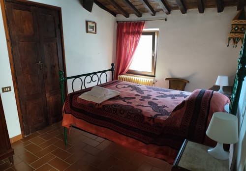 Rustikales Schlafzimmer im Agri-Bio Santa Palmira in Pomarance mit Schmiedeeisenbett, roter Bettwäsche, Holzbalken und roten Vorhängen.