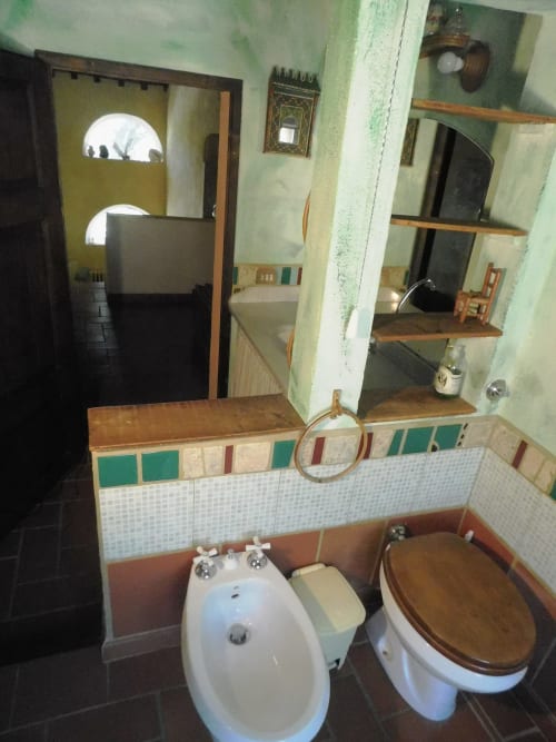 Badezimmer im Agri-Bio Santa Palmira in Pomarance mit Bidet, Toilette, Säulenwaschbecken, Holzregal und grünen Wandfliesen.
