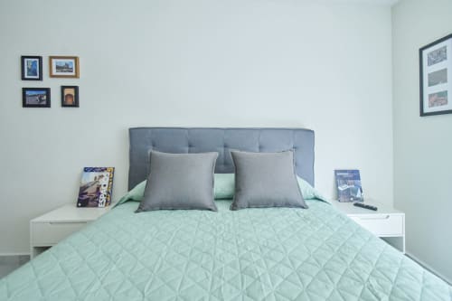 Moderno dormitorio en apartamento de Pares Homes en CDMX con cabecera tapizada gris, ropa de cama en menta y arte mural enmarcado.