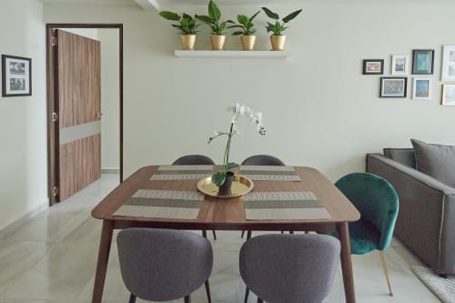 Sala de comedor de departamento moderno en CDMX con mesa de madera, sillas grises, orquídea blanca, plantas en maceta y sofá en Pares Homes