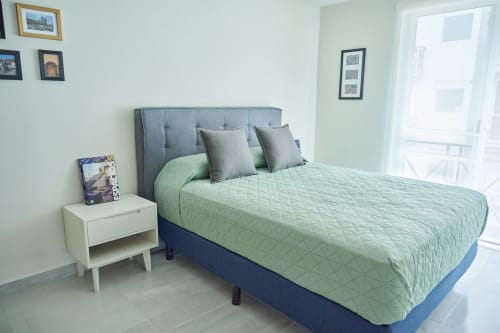 Habitación moderna en Pares Homes CDMX con ropa de cama verde acolchada, cabecera gris, mesita blanca y balcón