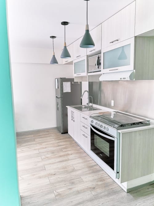 Cocina moderna en apartamento de CDMX con electrodomésticos de acero inoxidable, gabinetes blancos, pared acento menta e iluminación colgante