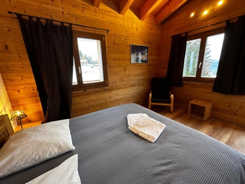 Chambre spacieuse en bois à La Tzoumaz avec lit double, vue montagne, rideaux noirs et équipements modernes