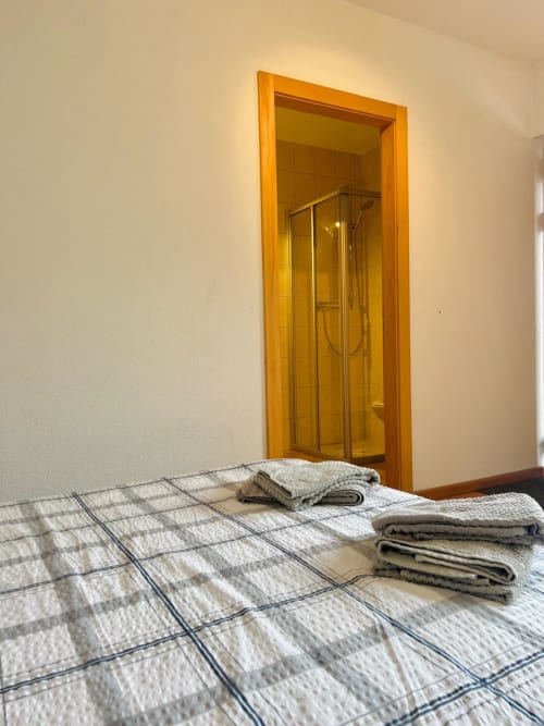 Chambre à l'auberge La Tzoum'hostel à La Tzoumaz avec serviettes pliées sur le lit et salle de bains attenante visible