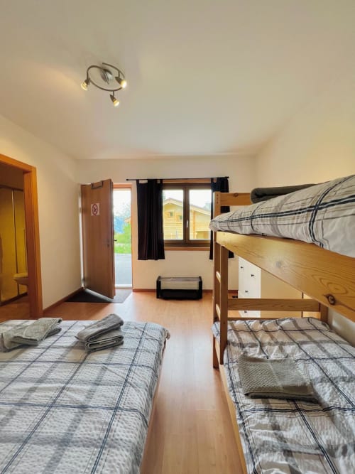 Chambre d'auberge lumineuse avec lits simples et superposés, mobilier en bois, fenêtres vue sur les montagnes de La Tzoumaz