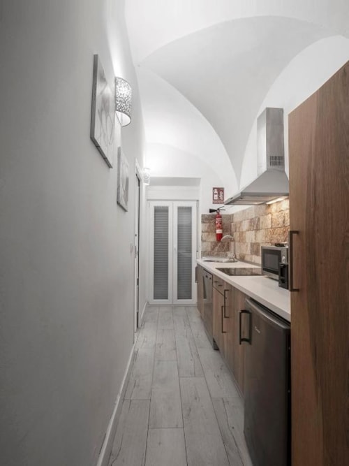 Cocina moderna con gabinetes de madera, salpicadero de piedra y techo abovedado blanco en departamento de Mérida
