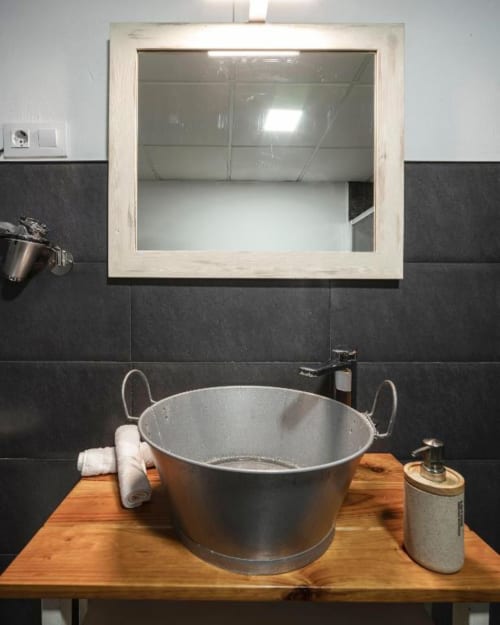 Moderno lavabo del apartamento Gestyp-AT en Mérida con cuenca metálica, mueble de madera y espejo enmarcado sobre fondo negro