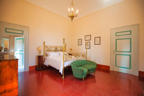 Camera elegante a Villa Ceci ad Andria con letto a quattro colonne in ottone, sedia verde decorata, pavimenti in cotto rosso