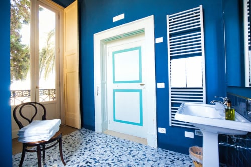 Camera Cristina, suite deluxe di Villa Ceci ad Andria con pareti blu vivaci, porta turchese, lavabo su piedistallo e giardino