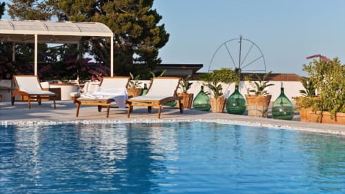 Terrazza piscina di Villa Ceci ad Andria con lettini, pergolato, sdraie e piante fiorite che affacciano sulla piscina blu