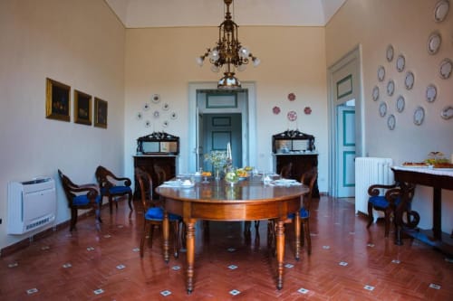 Elegante sala da pranzo di Villa Ceci con tavolo rotondo in legno, sedie blu, lampadario e piatti decorativi in esclusiva dimora