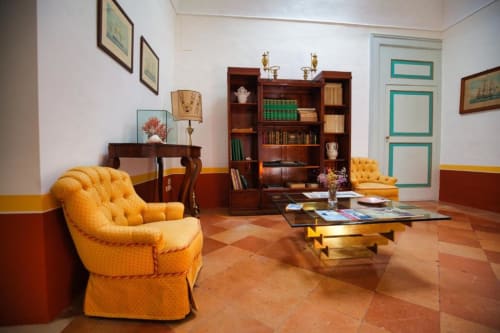 Elegante soggiorno di Villa Ceci B&B ad Andria con poltroncine gialle, libreria in legno e pavimento in cotto.