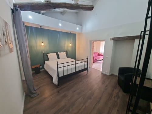 Camera spaziosa con letto in metallo nero, parete verde accent, travi a vista e accesso al salotto