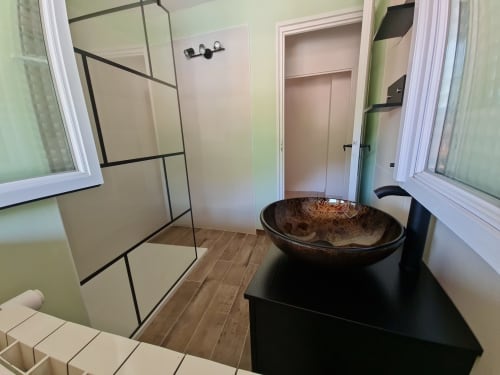 Bagno moderno con lavabo nero a forma di vaso, doccia aperta con divisorio in vetro e elementi in bianco