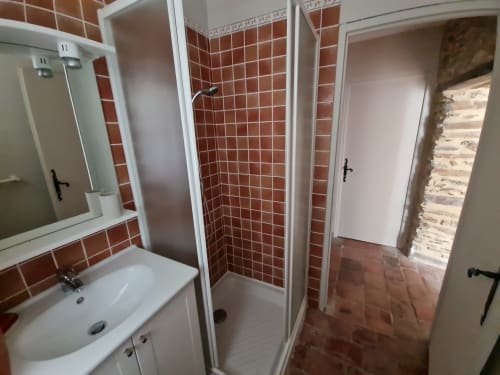 Bagno moderno con pareti in piastrelle rosse, lavandino bianco, specchio e cabina doccia in vetro presso il Gîte Le Tilleul B&B a Le Martinet